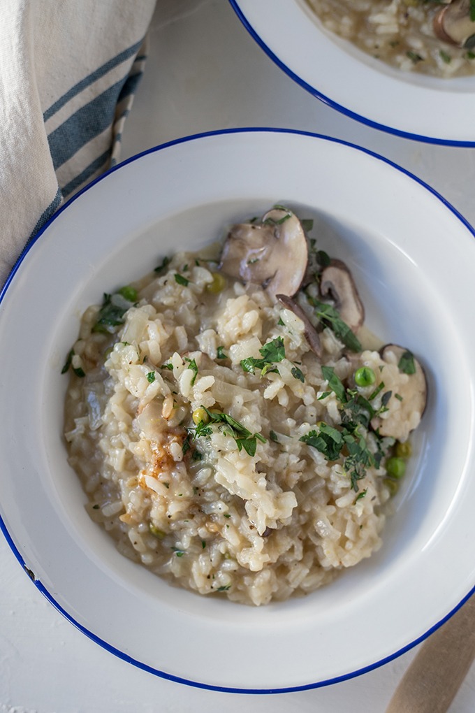 close up plate of mushroom pea risotto on a white enamel plate with blue rim