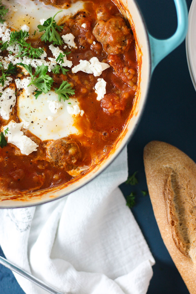 Close up spicy shakshuka on blue board, baguette loaf bottom right 