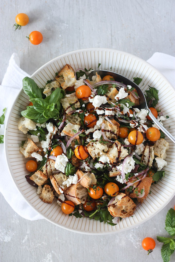 panzanella salad recipe ingredients in a white bowl surrounded by tomatoes and fresh mint