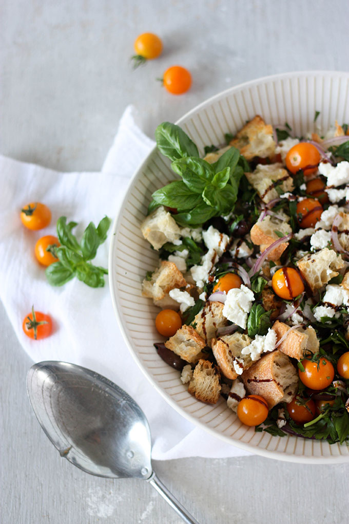 panzanella salad in white salad bowl, surrounded by tomatoes basil and an antique spoon