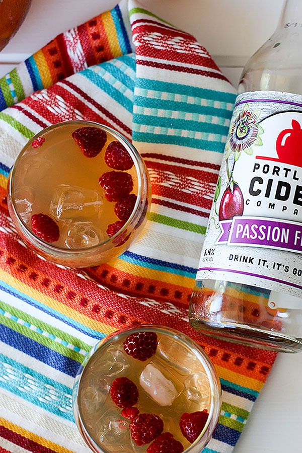 two glasses of passionfruit cider punch on multi coloured napkin, empty cider bottle to right of glasses