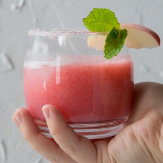 hand out holding a peach margarita in front of white board