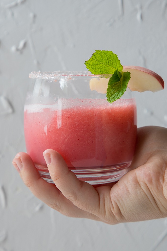 hand holding up peach margarita in front of white board