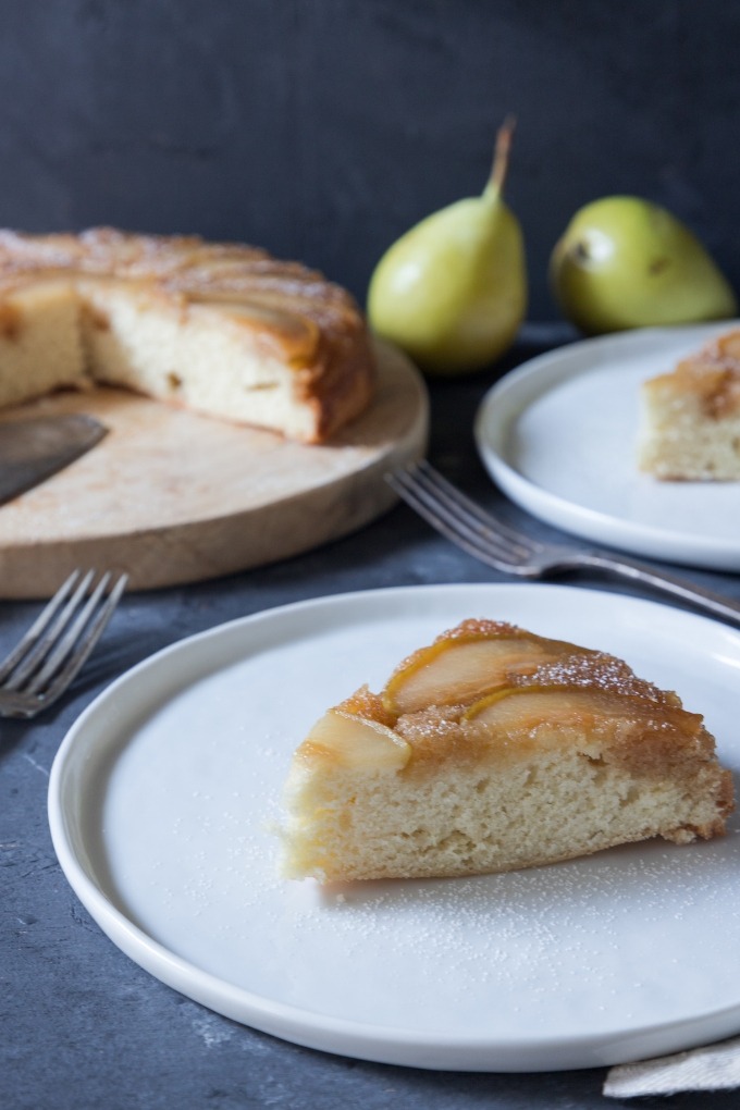 slice of pear upside-down cake on white plate with cake in background