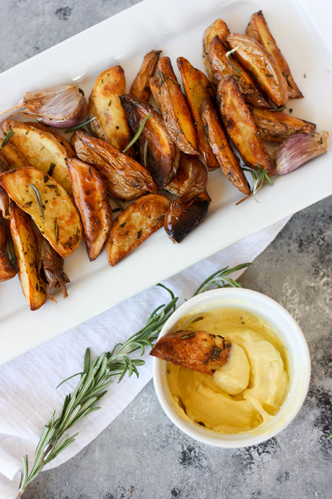 oven baked fries on white plate next to aioli dip with fry dipped in it