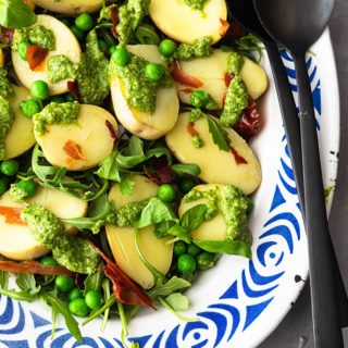 pesto potato salad on blue and white plate with black salad servers