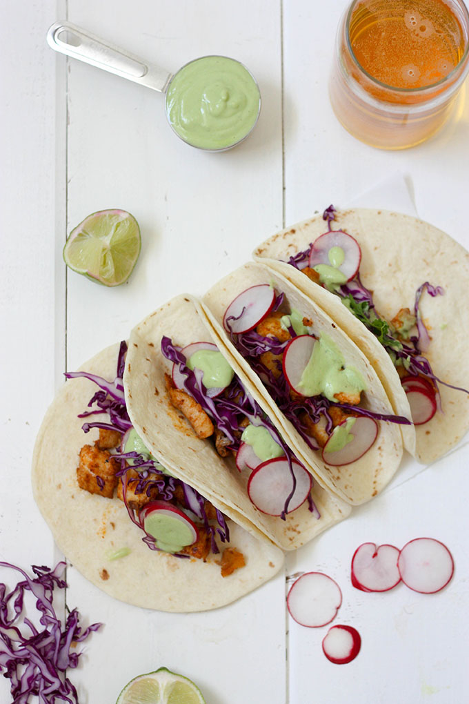 overhead view of healthy fish tacos, lime wedges on side, beer in glass and measuring cup full of dressing