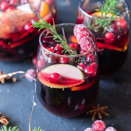 two glasses of red sangria with pitcher in background