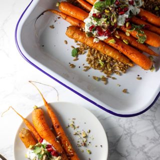 harissa roasted carrots on a white plate next to carrots in a blue and white enamel baking tray