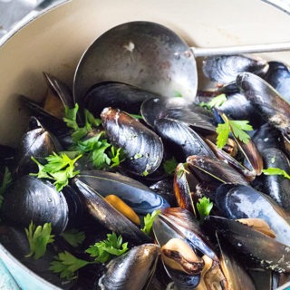 blue dutch oven with rosé mussles, antique scoop and garnished with parsley