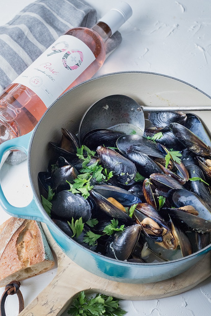 dutch oven pot of wine mussels on wooden antique board front of 90+ cellars bottle of rosé wine