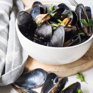 bowl of rosé mussels on an antique board next to a grey linen