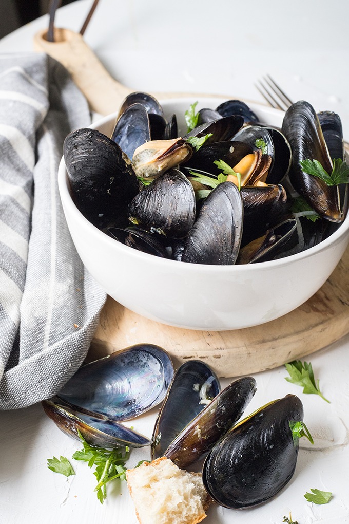 bowl of rosé mussels on an antique board next to a grey linen