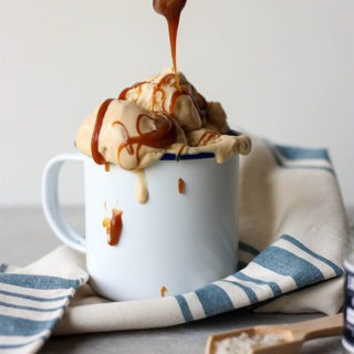 spoon drizzling caramel over a cup of no churn ice cream on a blue and white napkin