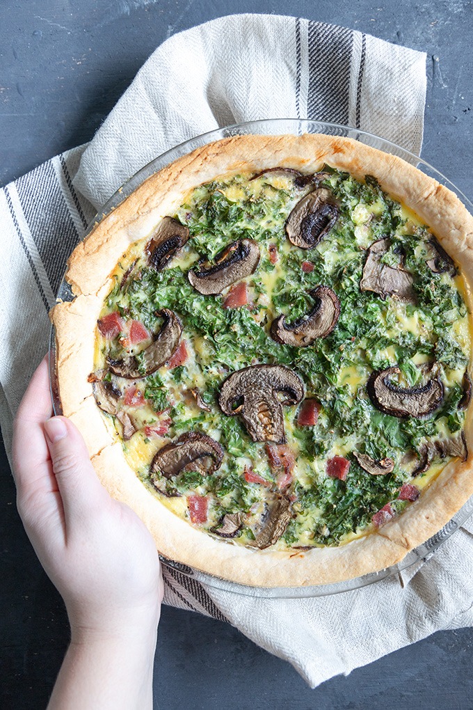 hand holding quiche in glass dish