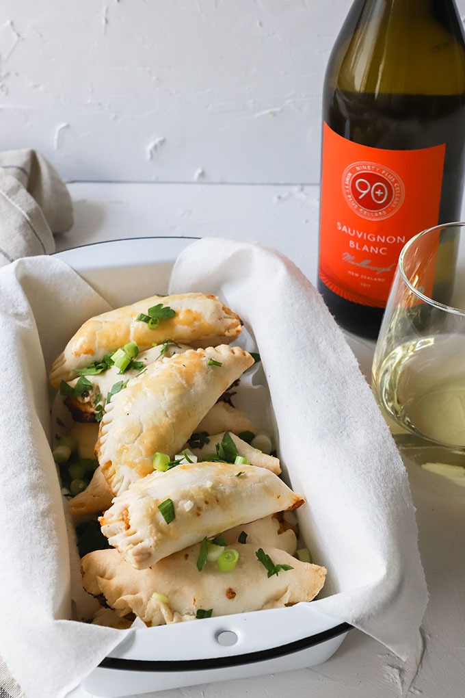 shrimp empanadas in an enamel loaf pan next to bottle and glass of white wine