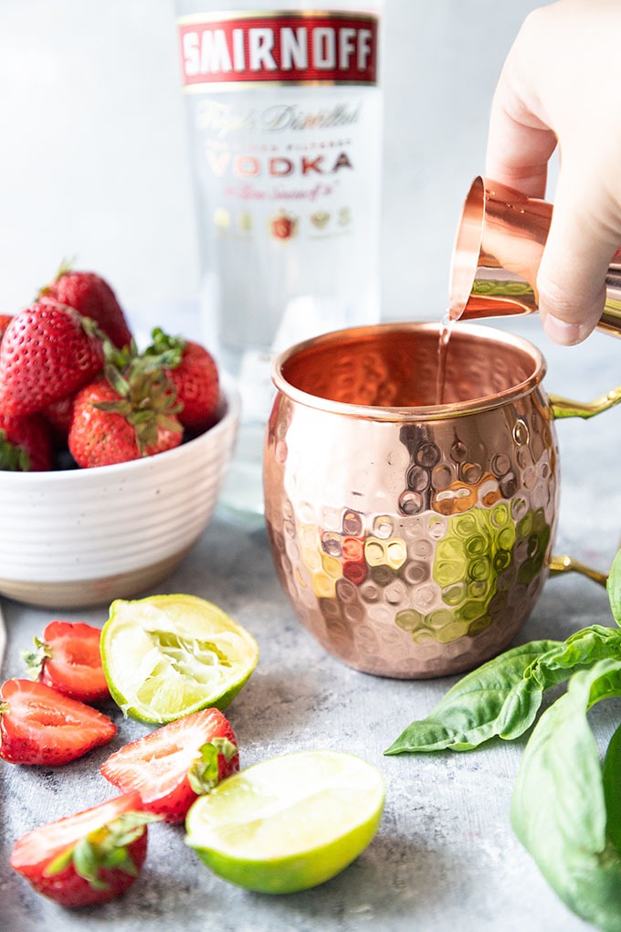 hand pouring a shot of vodka into a Moscow mule mug