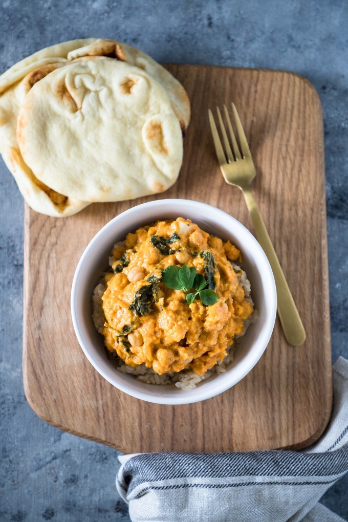 overhead sweet potato chickpea curry on wooden board with naan