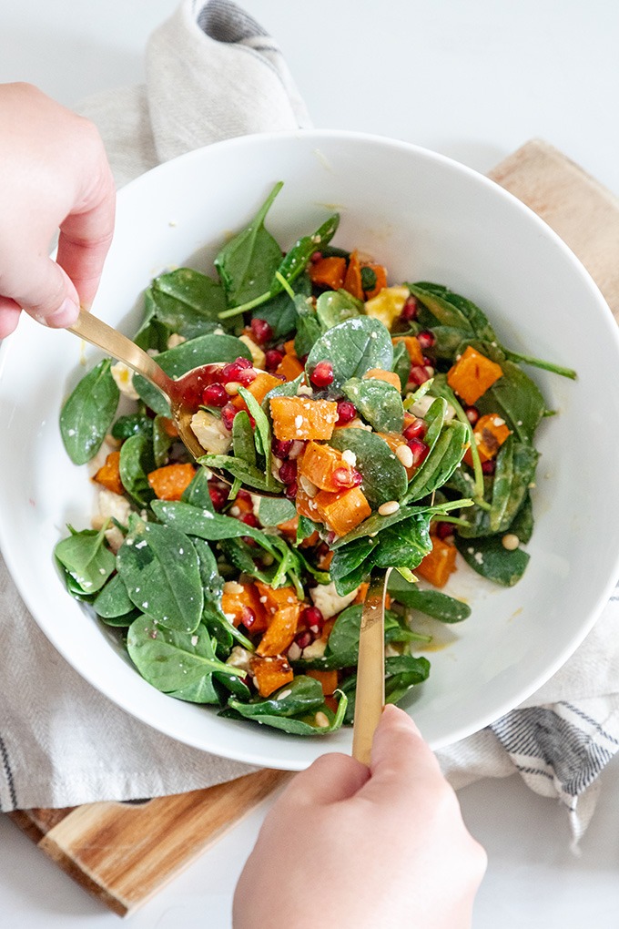 roasted sweet potato salad being tossed with gold salad servers