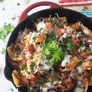 Red skillet full of pulled pork nachos on a brigh coloured towel