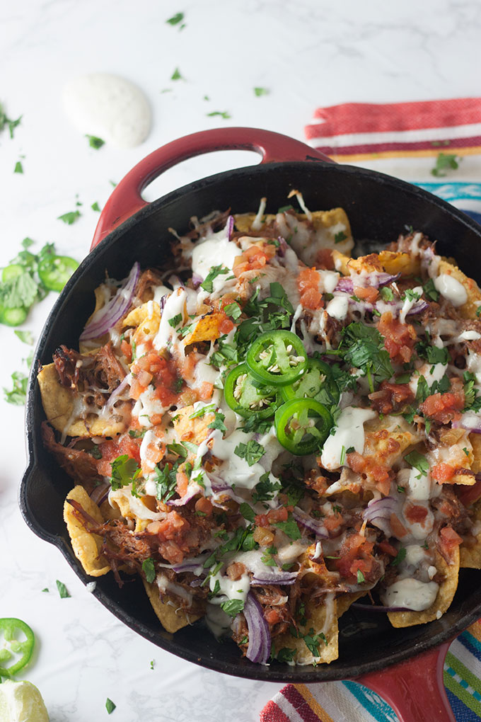 close up of pulled pork nachos in red skillet on colourful napkin