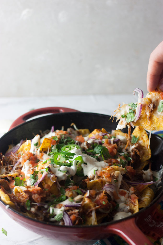 hand reaching out to take a nacho chip from red skillet