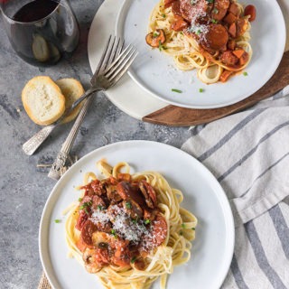 two plates of tomato chorizo pasta with red wine and antique forks