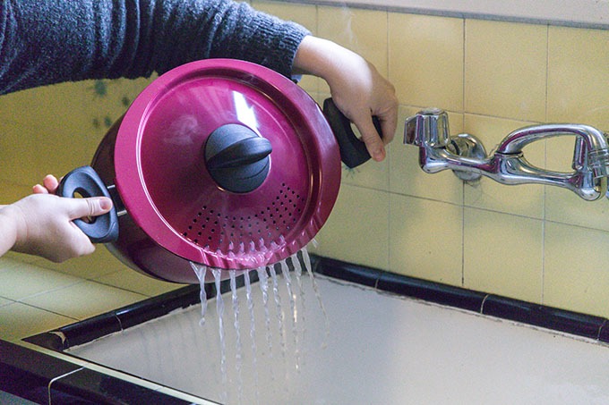 person holding Bialetti pasta pot draining it into a sink