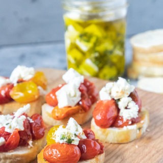 tomato crostini on wooden board in front of marinated feta