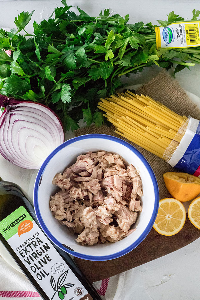 bowl of tuna, olive oil bottle, half a red onion, lemon wedges, fettucine and fresh parsley