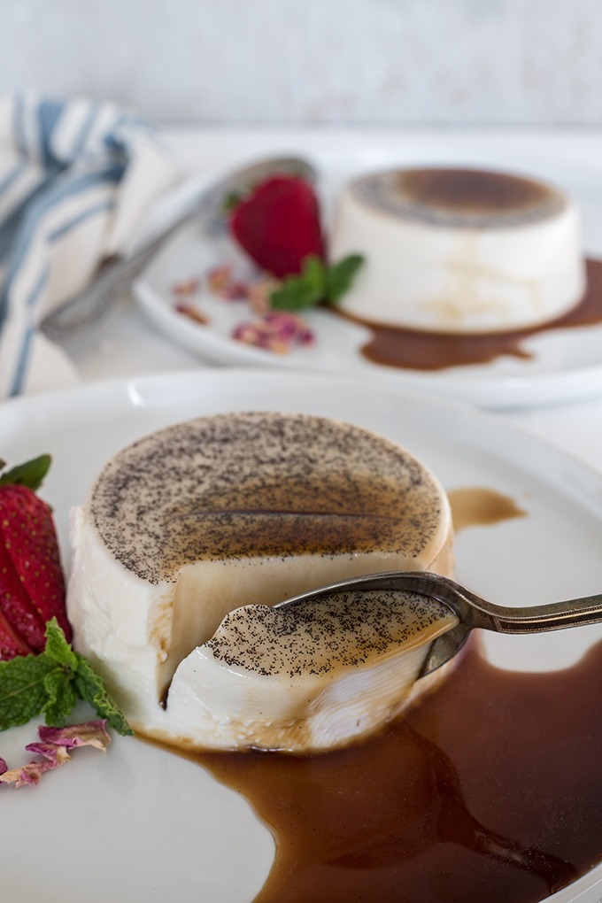 spoon taking a piece out of the vanilla panna cotta, panna cotta on white plate covered in espresso syrup