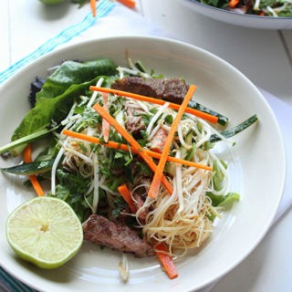 one bowl of vietnamese beef salad on a cream plate, garnished with lime wedge