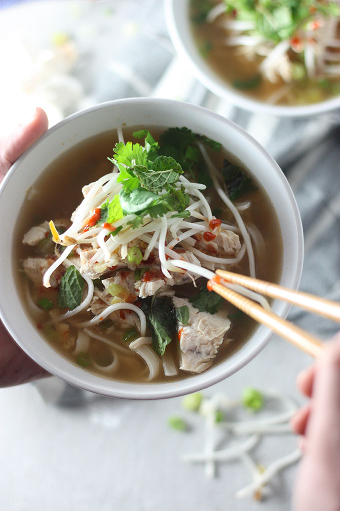 close up bowl of chicken pho, chopsticks reaching in to bowl