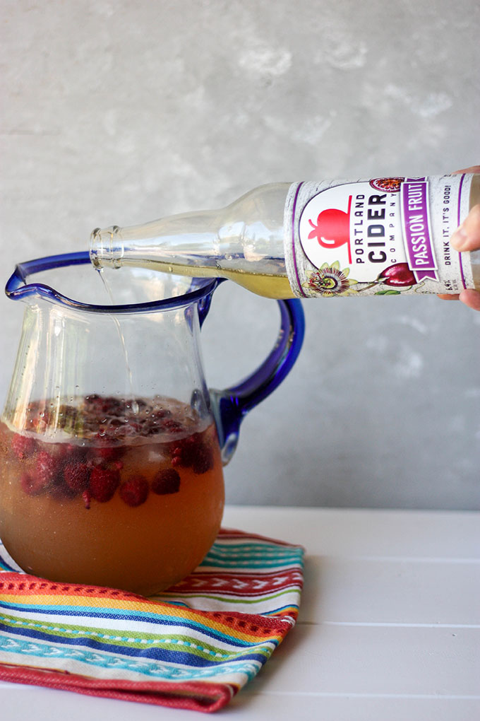 passionfruit cider being poured into a large pitcher of punch